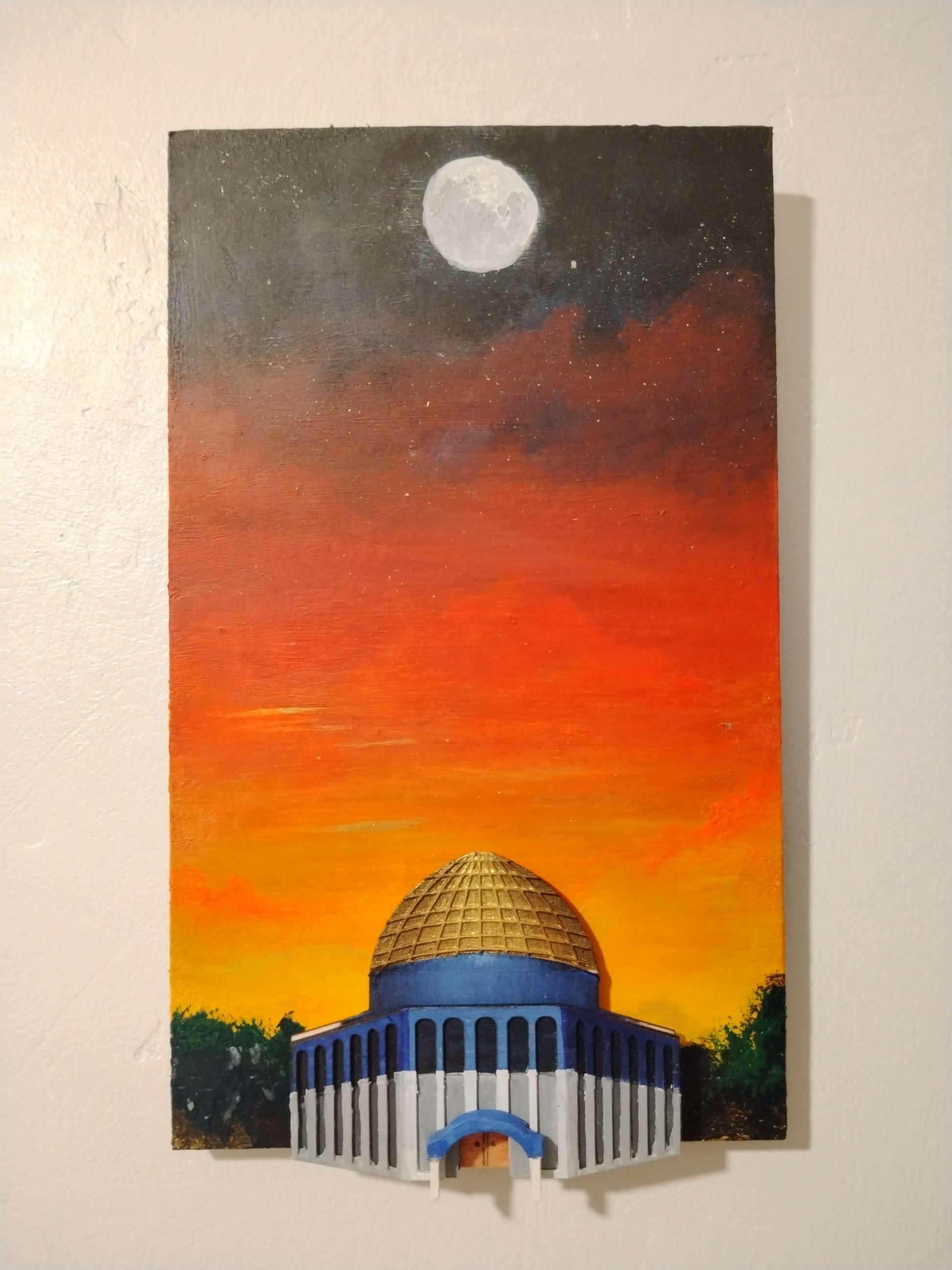 A vertical canvas painting of a domed building at sunset, with a bright moon in the dark sky above. The painting is mounted on a textured off-white wall.